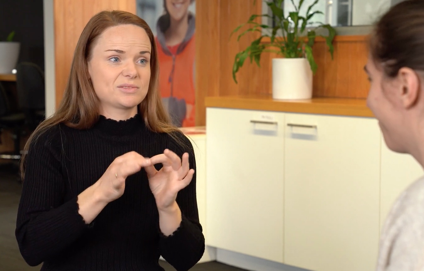 a screen-shot from the Skills and Jobs Centres information video. One woman is chatting with another woman in Auslan. She is making the sign for 'interpreter'.